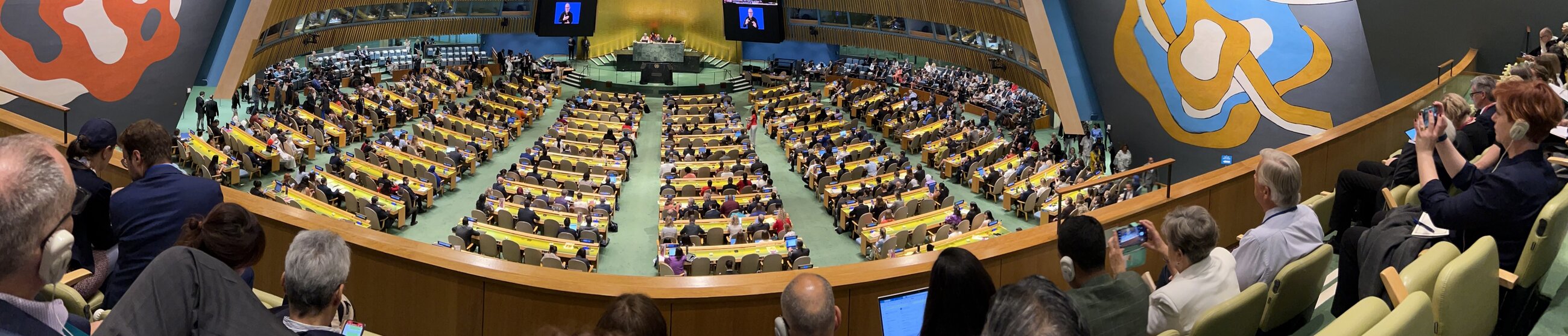 Panoramic view of a large conference hall filled with attendees seated in rows. A podium is at the center.