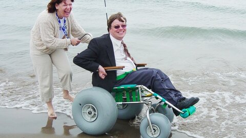 Happy woman pushing man in a beach wheelchair Thumbnail