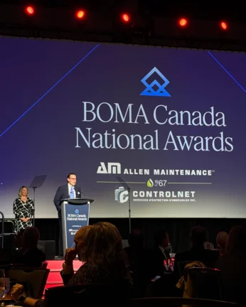 Person wearing a blue suite is on stage with a BOMA Canada Awards sign in the back and a ASL interpreter next to them