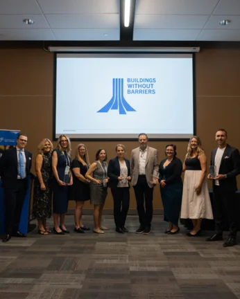 ten people stand up wearing eleant attire, some hold an award. There's a buildin without barriers logo behind them
