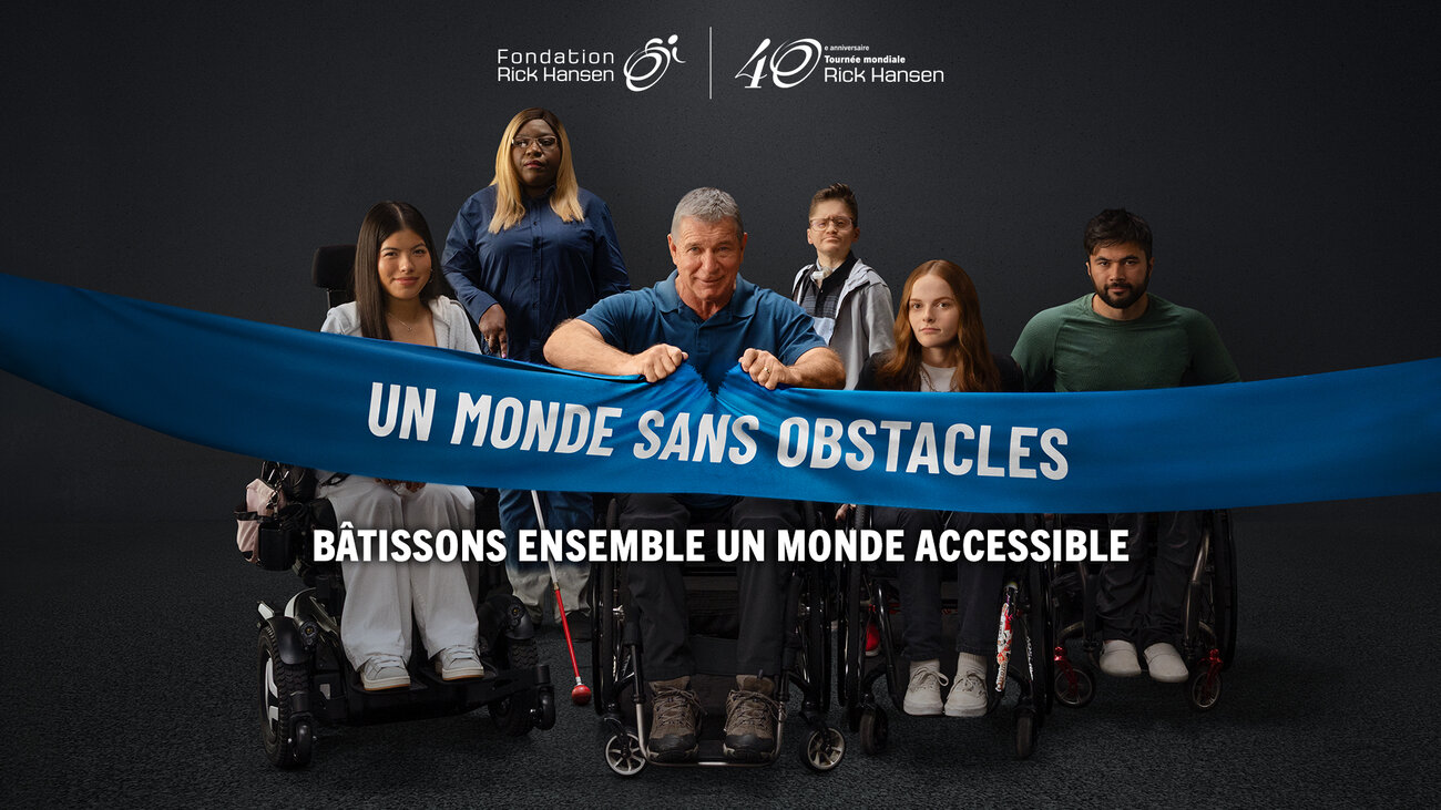 six people with visible mobility, vision, and hearing accessibility tools, including wheelchairs, a power wheelchair, a white cane, and hearing technology. A person at the centre grips a large blue banner reading “A World Without Barriers.” The Rick Hansen Foundation and 40th Anniversary Man In Motion World Tour logos appear above, with the text “Help Break Through Them All” below.