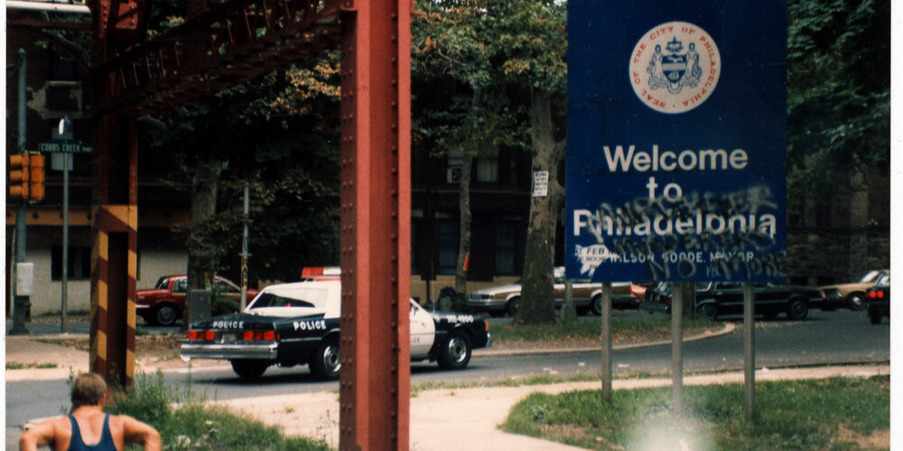 Rick Hansen wheels past welcome to Philadelphia sign in July of 1986.