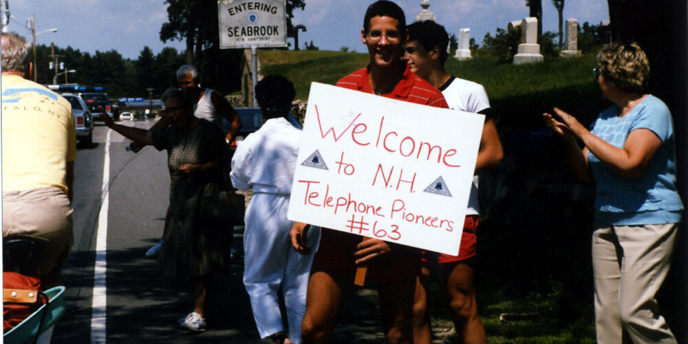 People in New Hampshire holding a sign quoting "Welcome to New Hampshire Telephone Pioneers # 63.