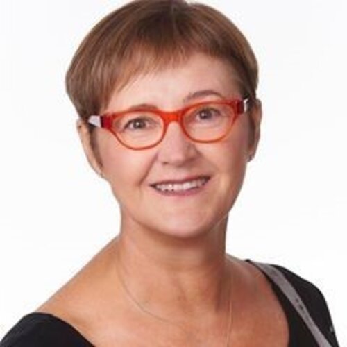 Woman with red short hair, wearing red glasses, smiling in black t-shirt. 