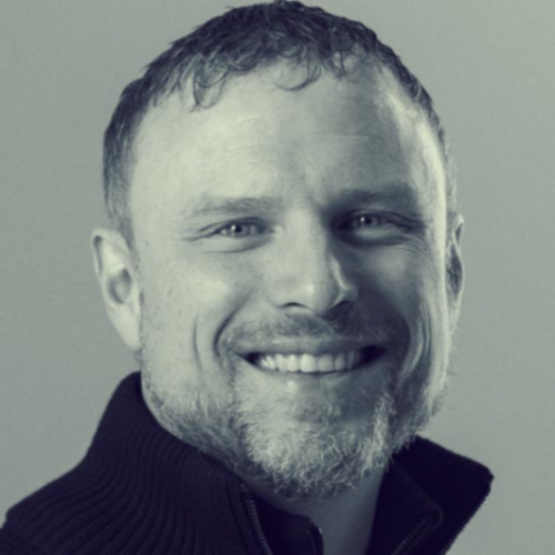 black and white headshot of a smiling man wearing a collared sweater