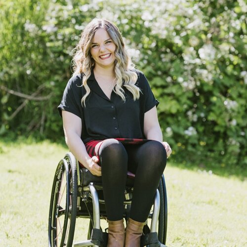 A woman with wavy blonde hair outdoors using a wheelchair