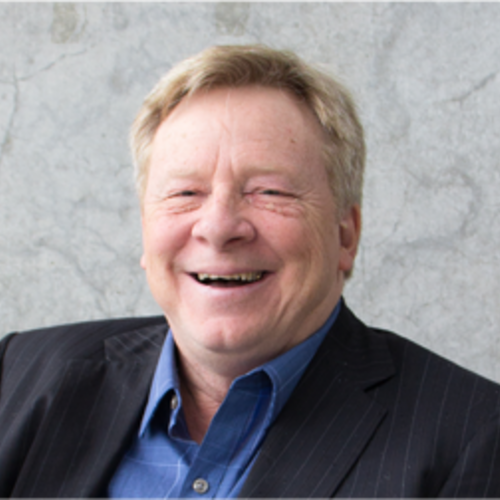 Middle aged man with short blonde hair, blue eyes smiling in a black blazer and blue button up shirt.  