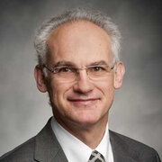Headshot, man wearing a suit and glasses, smiling