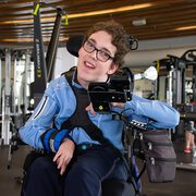 Young man with brown hair, wearing glasses using power wheel chair smiling. 