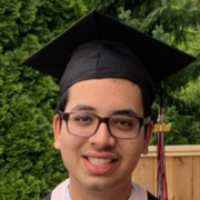 Youn man wearing glasses and graduation attire smiling at the camera