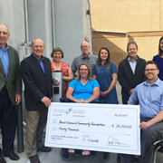 Group of people posing outdoors with an oversized check presented by the Rick Hansen Foundation. Two individuals in wheelchairs are positioned at the center of the group.
